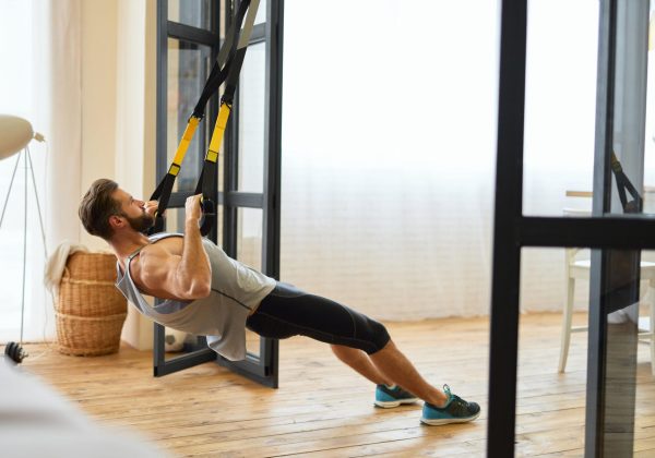Handsome bearded man in sportswear doing strength exercise with elastic fitness band